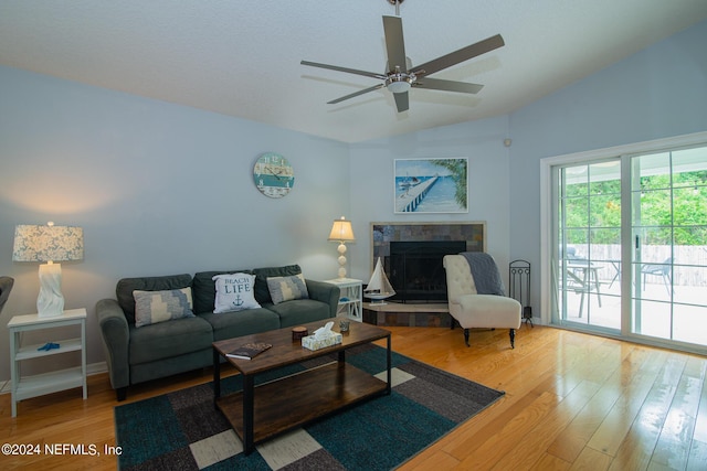 living room with hardwood / wood-style floors, ceiling fan, a tiled fireplace, and vaulted ceiling