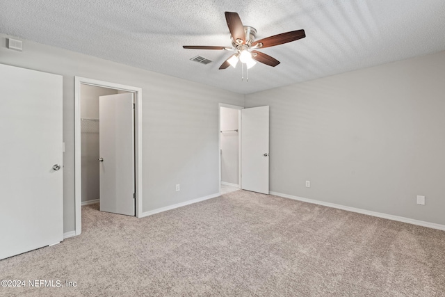 unfurnished bedroom featuring light carpet, a walk in closet, a textured ceiling, ceiling fan, and a closet