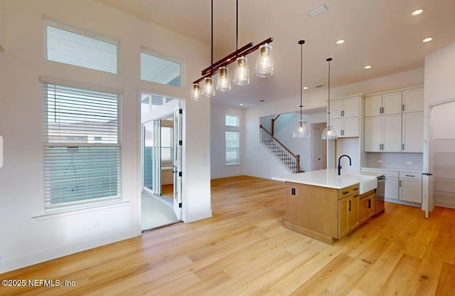 kitchen featuring light wood-style floors, white cabinets, a sink, and hanging light fixtures