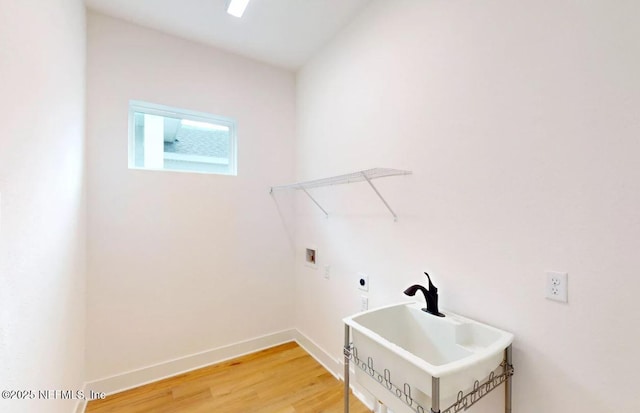 clothes washing area featuring hookup for a washing machine, laundry area, a sink, baseboards, and light wood finished floors