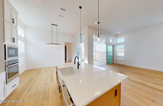 kitchen with light wood-style flooring, visible vents, light countertops, appliances with stainless steel finishes, and a center island with sink