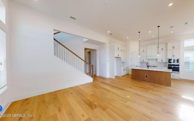 unfurnished living room featuring light wood-type flooring, visible vents, stairway, and recessed lighting