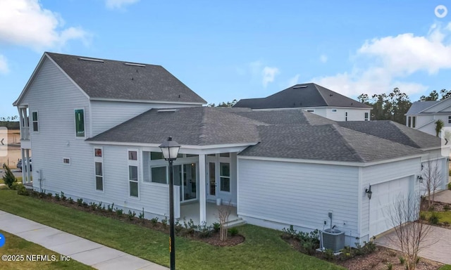 traditional home with a garage, central AC unit, a front yard, and a shingled roof