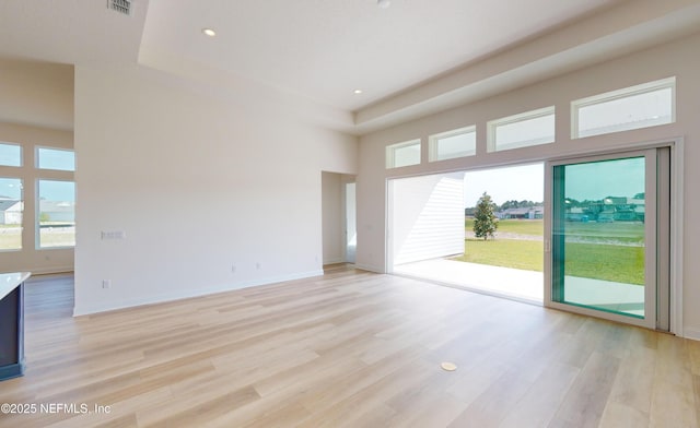 empty room with a tray ceiling, a towering ceiling, and light hardwood / wood-style floors