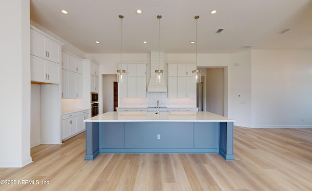 kitchen with a spacious island, sink, hanging light fixtures, light hardwood / wood-style floors, and white cabinetry