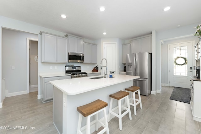 kitchen featuring a breakfast bar area, light countertops, appliances with stainless steel finishes, a kitchen island with sink, and a sink