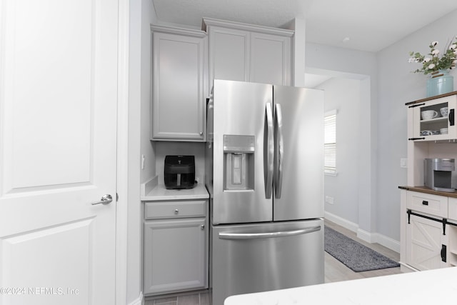 kitchen featuring gray cabinetry, light countertops, baseboards, and stainless steel fridge with ice dispenser