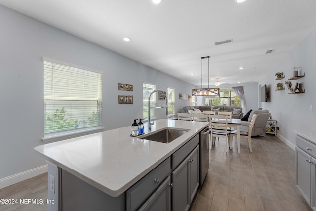 kitchen featuring a sink, visible vents, open floor plan, dishwasher, and a center island with sink