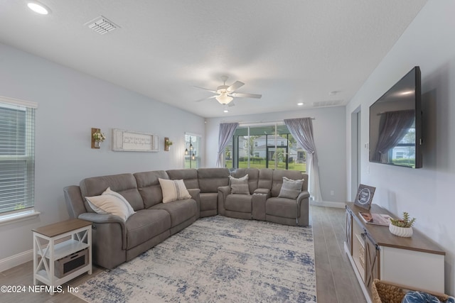 living room featuring light wood-style floors, ceiling fan, visible vents, and baseboards