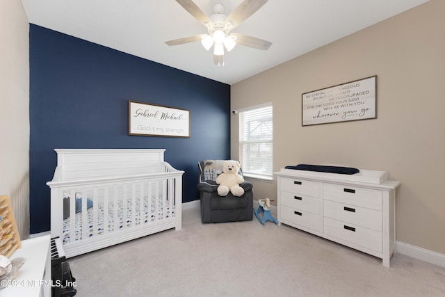 bedroom with a nursery area, baseboards, a ceiling fan, and light colored carpet