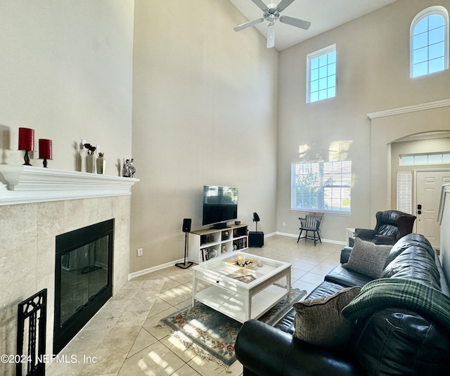 living room featuring light tile patterned floors, ceiling fan, a high ceiling, and a tiled fireplace