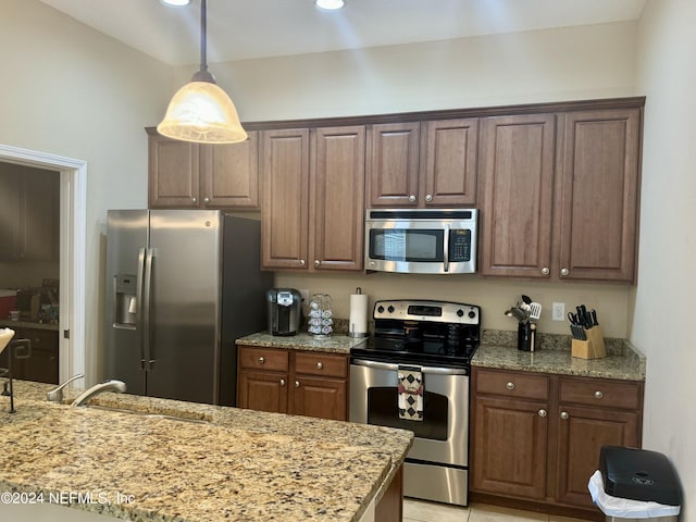 kitchen with pendant lighting, sink, light tile patterned floors, light stone counters, and stainless steel appliances