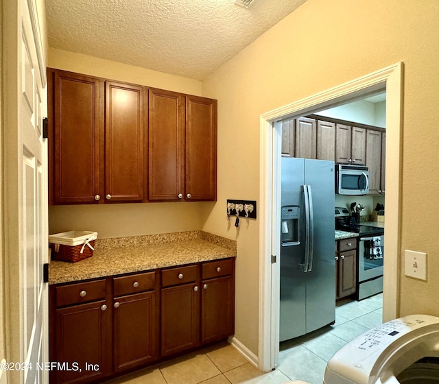 kitchen featuring light stone countertops, light tile patterned flooring, a textured ceiling, and appliances with stainless steel finishes