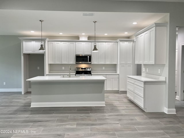 kitchen with sink, decorative light fixtures, stainless steel appliances, and a center island with sink