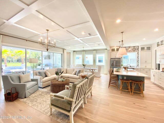 living room with sink, light hardwood / wood-style flooring, coffered ceiling, and a notable chandelier