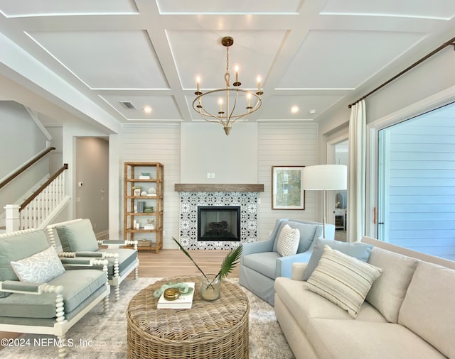 living room with a tile fireplace, light wood-type flooring, coffered ceiling, and an inviting chandelier