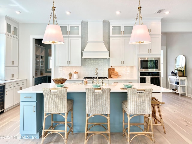 kitchen featuring custom exhaust hood, white cabinetry, and a kitchen island with sink