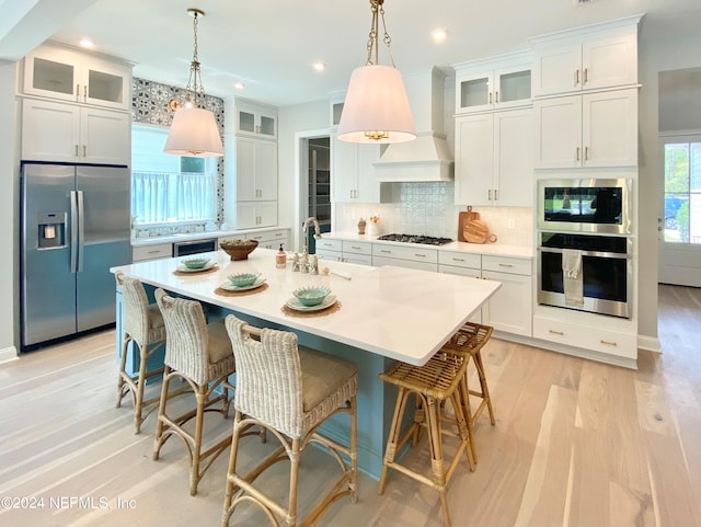 kitchen with stainless steel appliances, white cabinetry, premium range hood, and a center island with sink