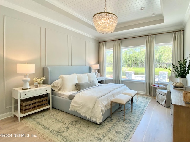 bedroom with a chandelier, a raised ceiling, ornamental molding, and light hardwood / wood-style flooring