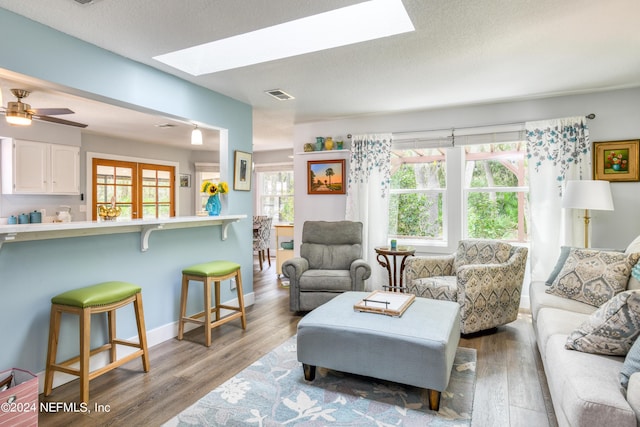 living room with a textured ceiling, a skylight, light hardwood / wood-style flooring, and ceiling fan