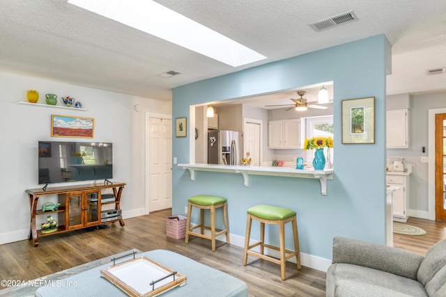 living room with a skylight, ceiling fan, dark hardwood / wood-style flooring, and a textured ceiling