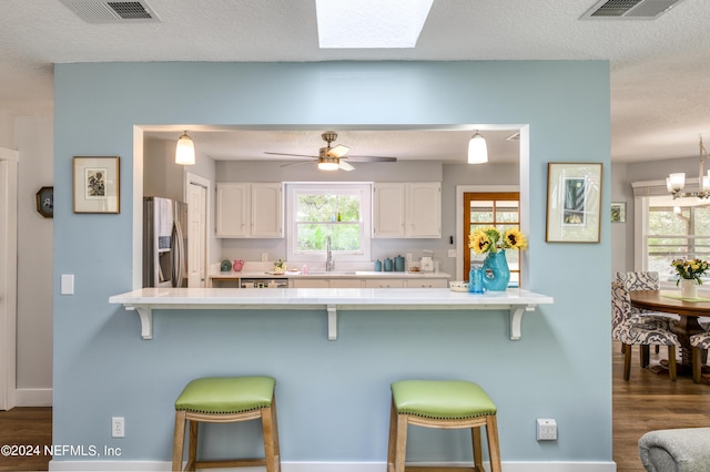 kitchen featuring stainless steel fridge, a kitchen breakfast bar, white cabinetry, and a healthy amount of sunlight