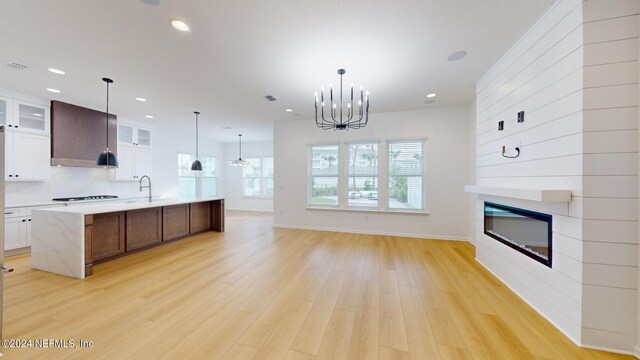 kitchen with white cabinets, an inviting chandelier, light wood-type flooring, and an island with sink