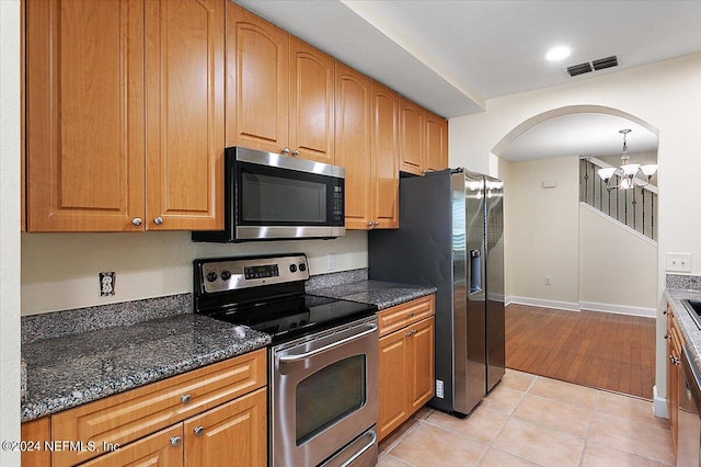 kitchen with light tile patterned flooring, appliances with stainless steel finishes, dark stone counters, hanging light fixtures, and a notable chandelier