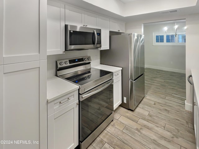 kitchen featuring white cabinets, appliances with stainless steel finishes, light hardwood / wood-style flooring, and light stone counters