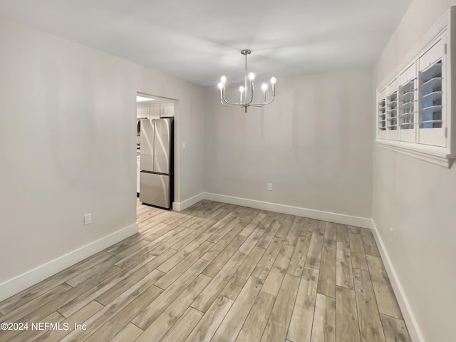 spare room with light hardwood / wood-style flooring and a chandelier