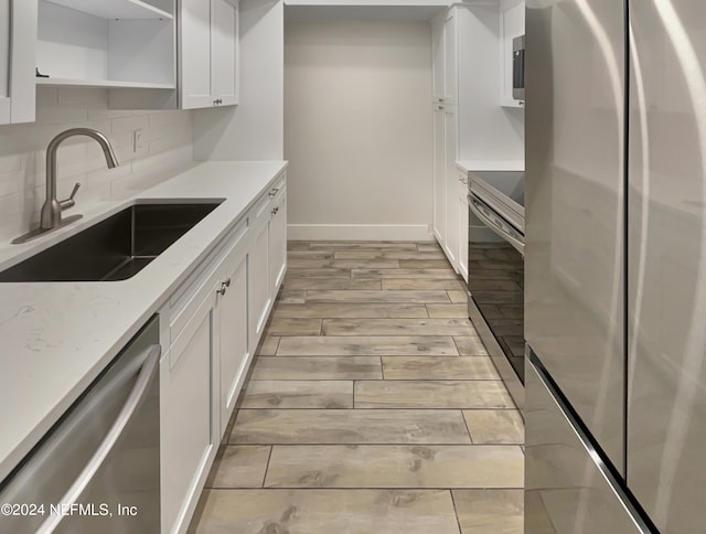 kitchen featuring light stone countertops, appliances with stainless steel finishes, sink, light hardwood / wood-style floors, and white cabinetry