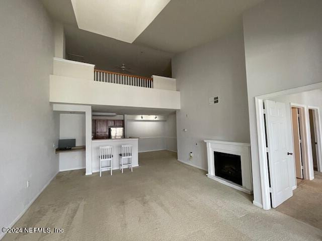 unfurnished living room featuring light colored carpet and a high ceiling