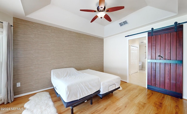 bedroom featuring hardwood / wood-style flooring, ceiling fan, a barn door, and a raised ceiling