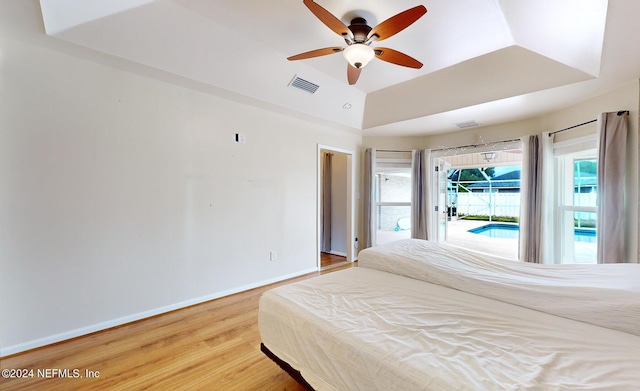 bedroom with wood-type flooring, lofted ceiling, access to exterior, ceiling fan, and a raised ceiling