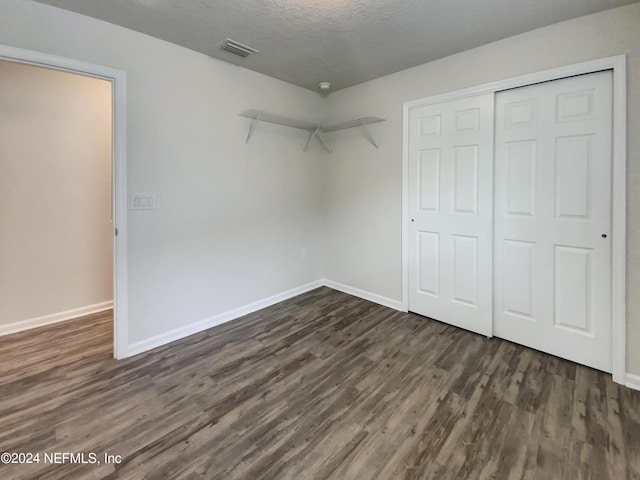 unfurnished bedroom featuring a textured ceiling, dark wood-type flooring, and a closet