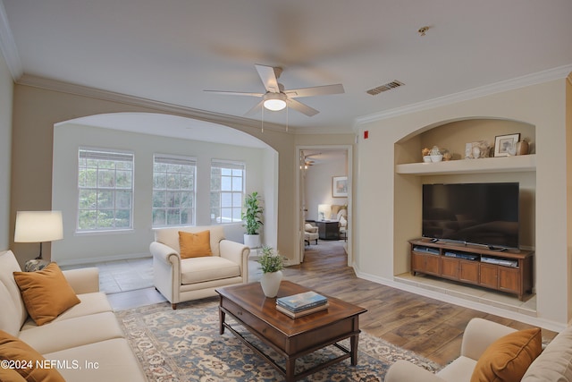 living room featuring built in shelves, crown molding, ceiling fan, and light hardwood / wood-style floors