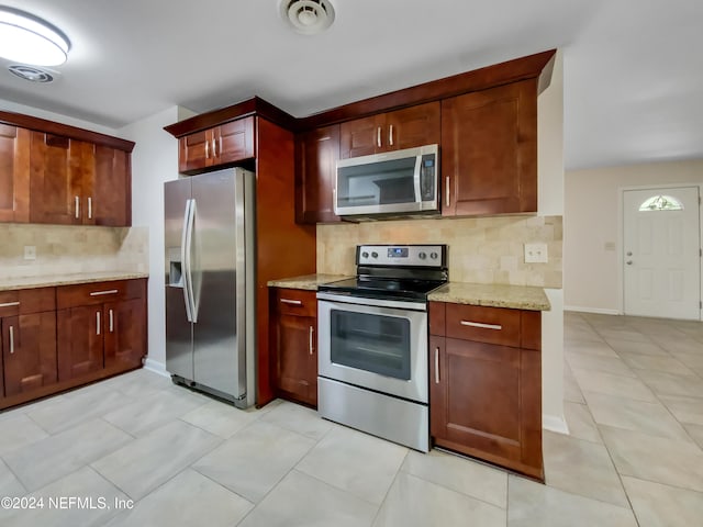 kitchen featuring light tile patterned floors, light stone countertops, appliances with stainless steel finishes, and tasteful backsplash