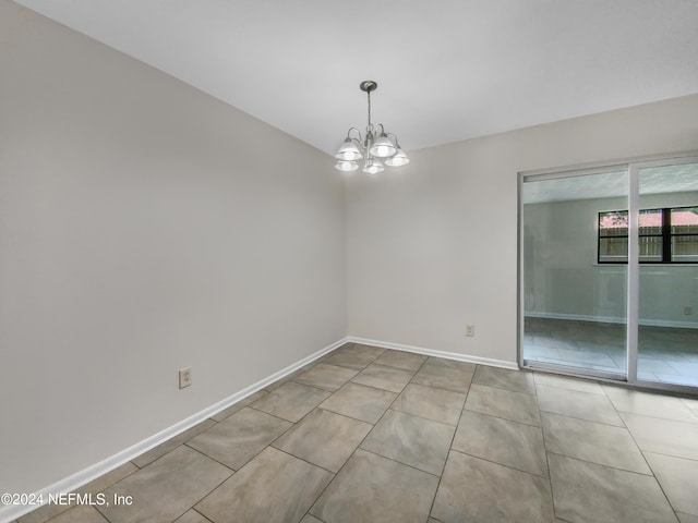 tiled spare room featuring an inviting chandelier