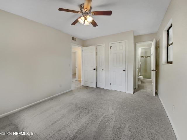 unfurnished bedroom featuring ceiling fan, light colored carpet, ensuite bathroom, and two closets