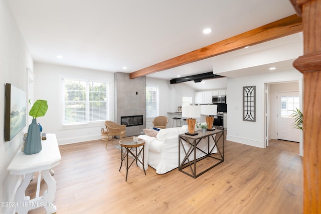 living room featuring light wood-style flooring, baseboards, beam ceiling, and a tile fireplace