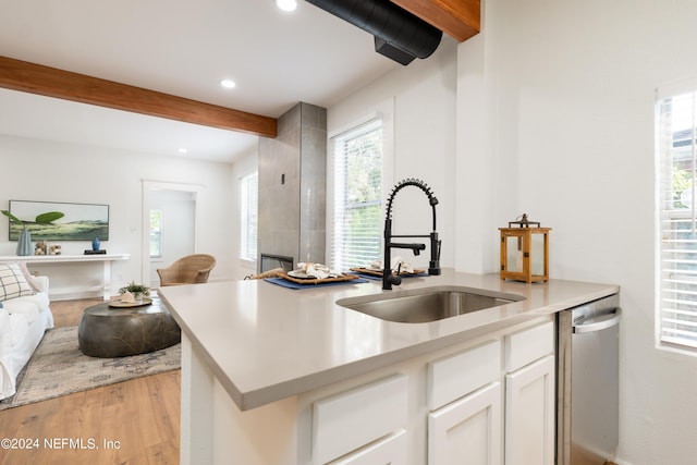 kitchen with light wood finished floors, dishwasher, open floor plan, beamed ceiling, and a sink