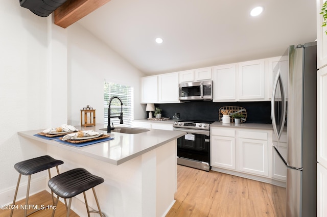 kitchen with vaulted ceiling with beams, appliances with stainless steel finishes, white cabinets, a sink, and a kitchen breakfast bar