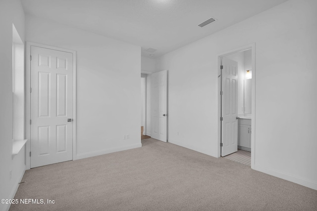 unfurnished bedroom with light colored carpet and connected bathroom