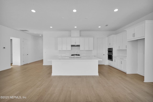 kitchen with light wood-type flooring, white cabinetry, and a center island with sink