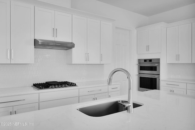 kitchen featuring light stone countertops, white cabinets, stainless steel appliances, tasteful backsplash, and sink