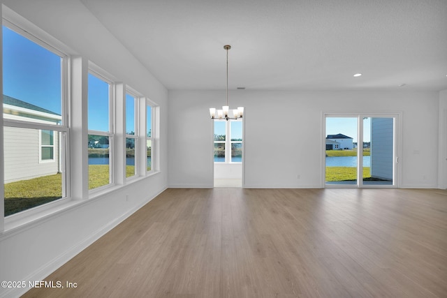 spare room featuring a chandelier, light hardwood / wood-style flooring, and a water view