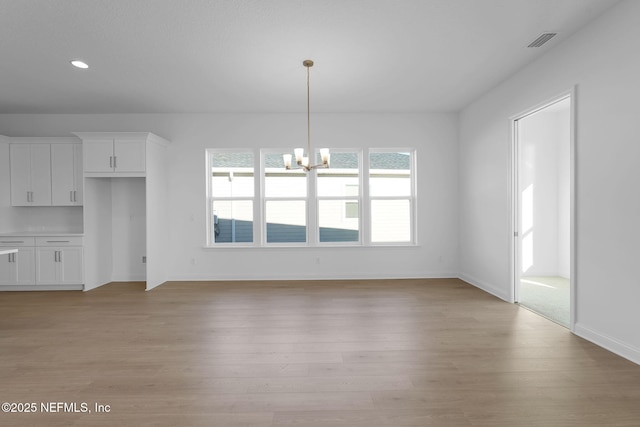 unfurnished living room with an inviting chandelier and light hardwood / wood-style floors