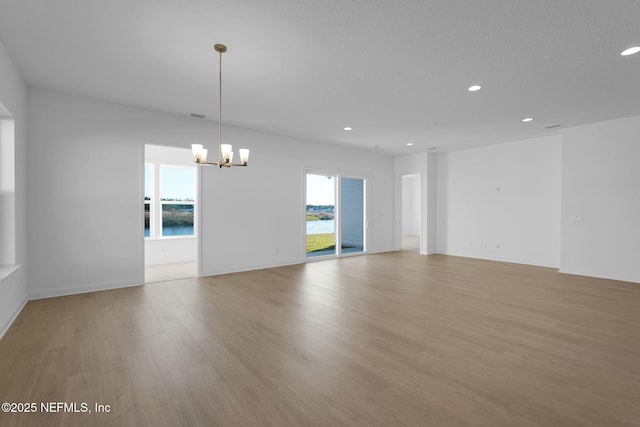 spare room featuring plenty of natural light, a chandelier, and light hardwood / wood-style floors