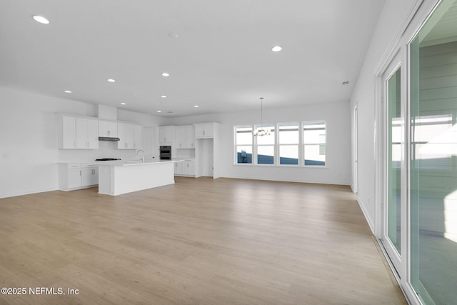 unfurnished living room featuring light wood-type flooring, sink, and a chandelier