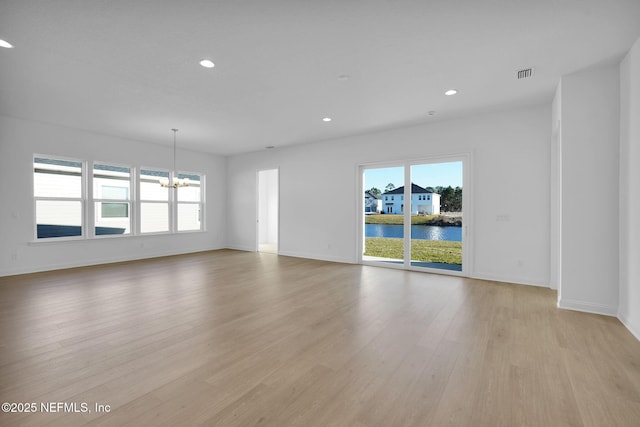 empty room featuring a water view, a chandelier, and light hardwood / wood-style flooring